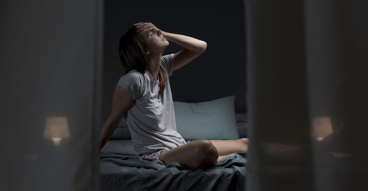 Tired woman suffering from heat sits in bed at night.