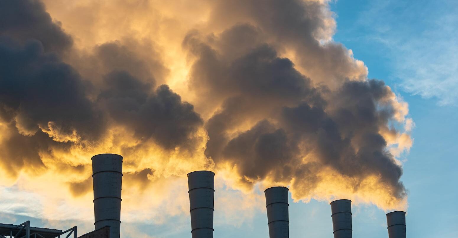 Industrial chimneys spewing smoke and soot in the blue sky polluting the air and contributing to climate change.