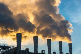 Industrial chimneys spewing smoke and soot in the blue sky polluting the air and contributing to climate change.