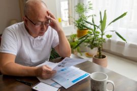 A senior man holding his head trying to cope the raising cost of energy and tax bills