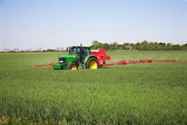 A tractor-drawn applicator applies nitrogen granule fertiliser to a field of corn.