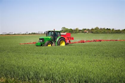 A tractor-drawn applicator applies nitrogen granule fertiliser to a field of corn.