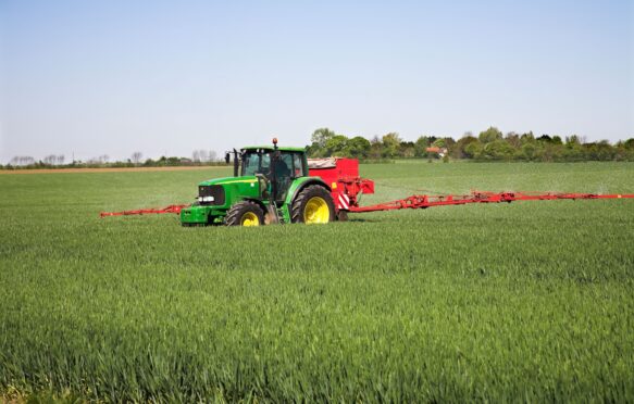 A tractor-drawn applicator applies nitrogen granule fertiliser to a field of corn.