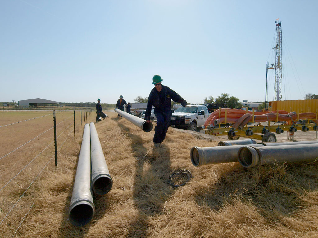 Workers bring water pipes to a well site as they prepare for hydraulic fracturing